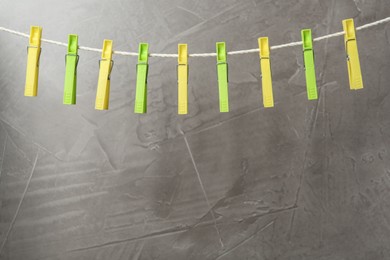 Photo of Colorful plastic clothespins on rope against grey stone background. Space for text