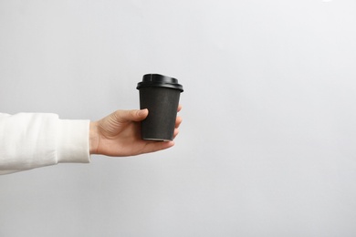 Woman holding takeaway paper coffee cup on light background. Space for text