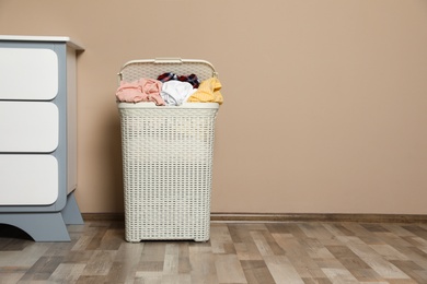 Photo of Plastic laundry basket with dirty clothes near color wall in room. Space for text
