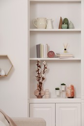 Photo of Stylish shelves with decorative elements and houseplants near white wall. Interior design