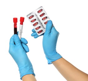 Photo of Scientist in protective gloves holding pills and test tubes of blood samples with label Covid-19 on white background, closeup