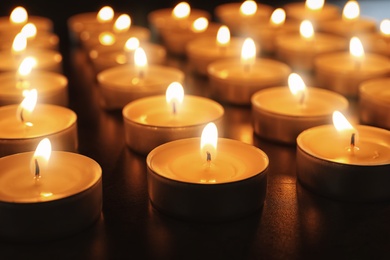 Photo of Wax candles burning on table in darkness, closeup