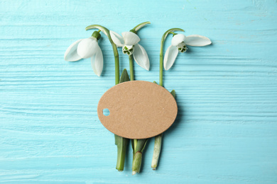 Photo of Fresh spring snowdrop flowers and blank card on blue wooden table, flat lay. Space for text