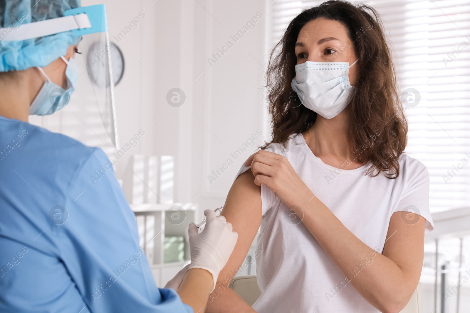 Photo of Doctor vaccinating mature woman against Covid-19 in clinic