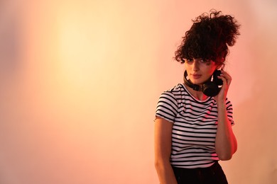 Photo of Beautiful young woman with headphones on color background in neon lights. Space for text