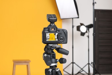 Photo of Camera on tripod, bar stool and professional lighting equipment in modern photo studio