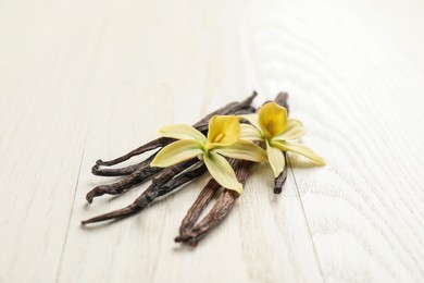 Photo of Beautiful vanilla flowers and sticks on white wooden table, closeup