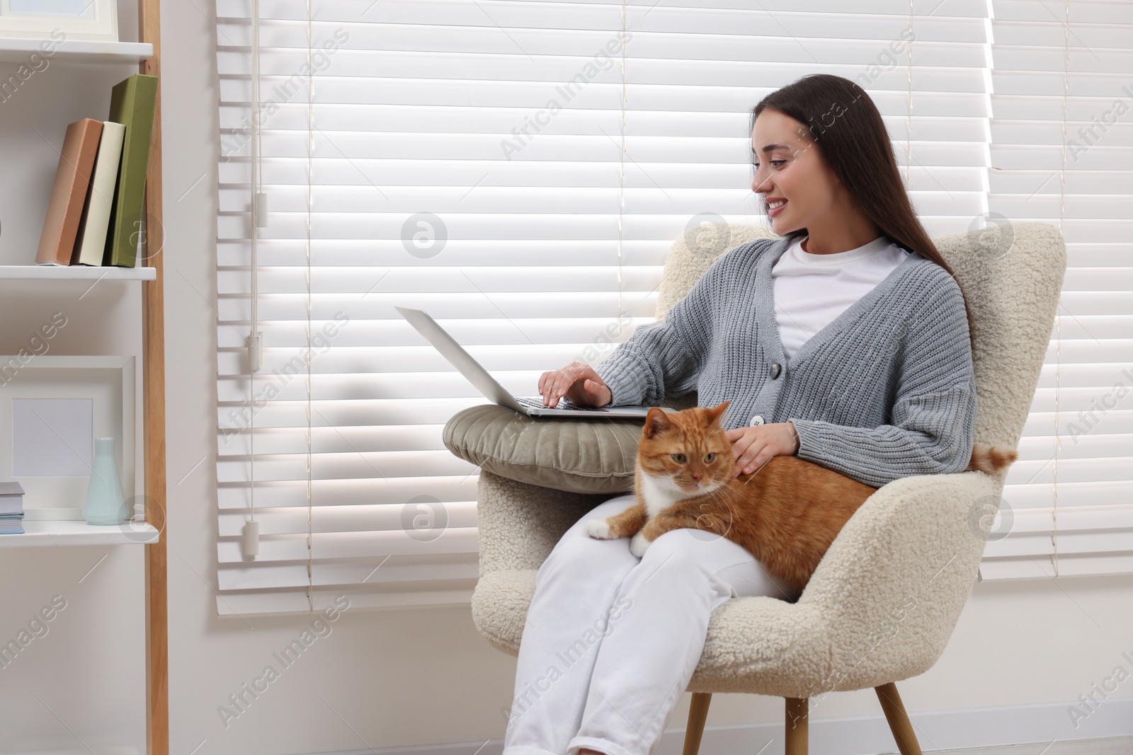 Photo of Happy woman working with laptop and petting cute cat at home