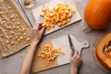 Photo of Woman with knife taking piece of fresh pumpkin at light grey table, top view
