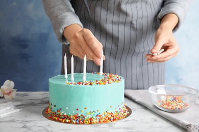 Photo of Woman decorating fresh delicious birthday cake with candles at table, closeup