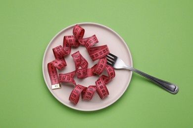 Photo of Measuring tape and fork on light green background, top view. Weight loss concept