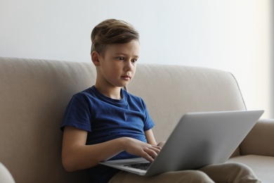 Photo of Shocked little child with laptop on sofa in room. Danger of internet
