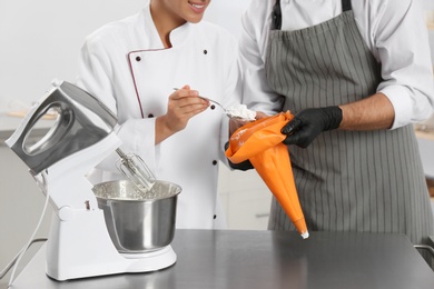 Photo of Pastry chefs preparing cream at table in kitchen, closeup