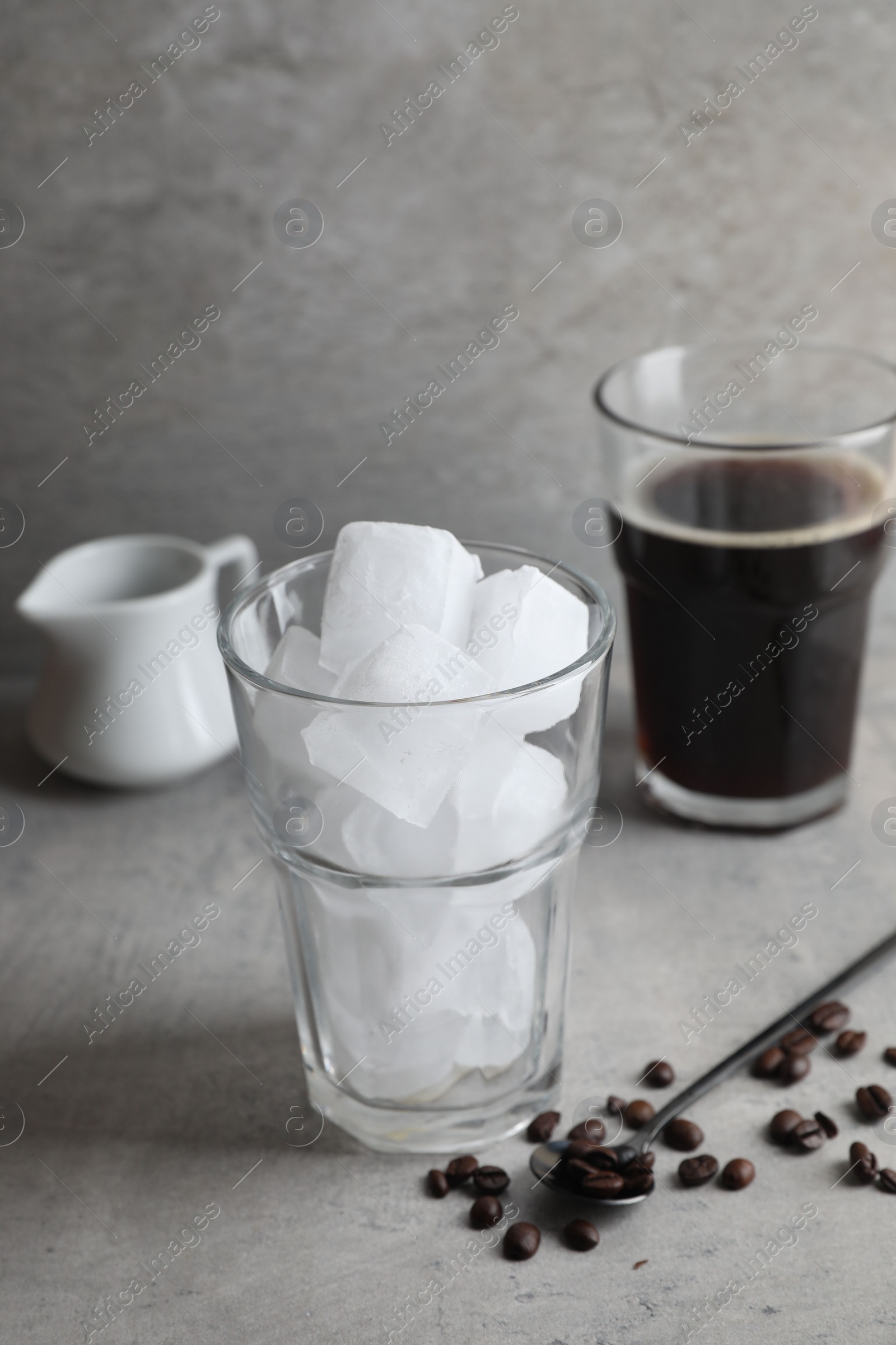 Photo of Making iced coffee. Ice cubes in glass, ingredients and spoon on gray table