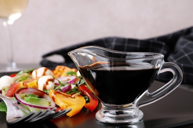 Photo of Gravy boat of balsamic vinegar on plate with vegetable salad, closeup