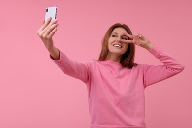 Beautiful woman taking selfie on pink background