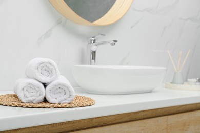 Rolled bath towels on white table in bathroom, space for text