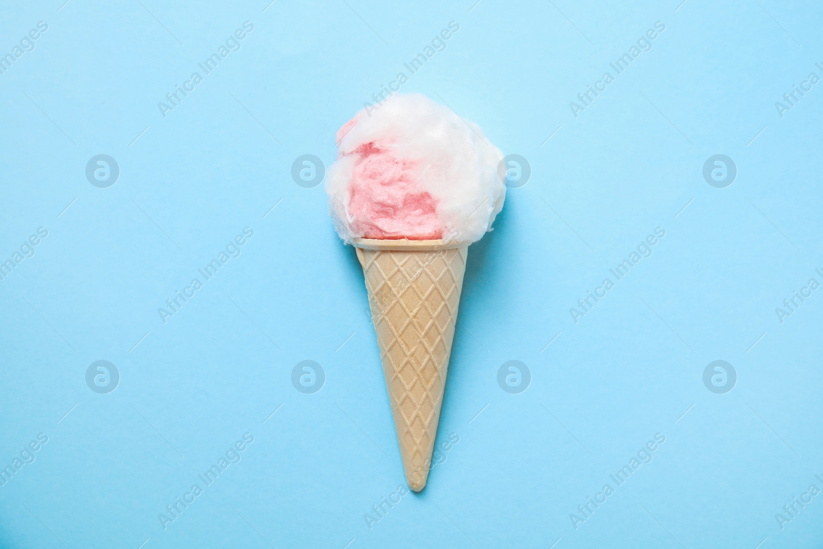 Photo of Ice cream cone with fluffy cotton candy on color background, top view