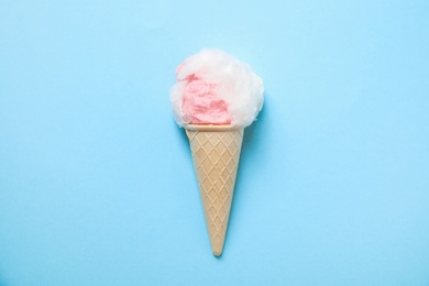 Ice cream cone with fluffy cotton candy on color background, top view