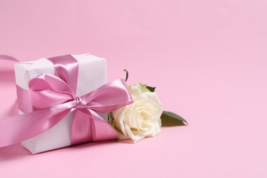 Photo of Gift box and beautiful rose flower on pink background, space for text