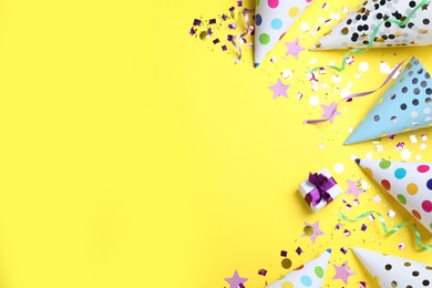 Photo of Flat lay composition with party hats, gift box and confetti on yellow background, space for text. Birthday decor