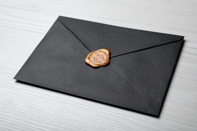 Photo of Black envelope with wax seal on white wooden background