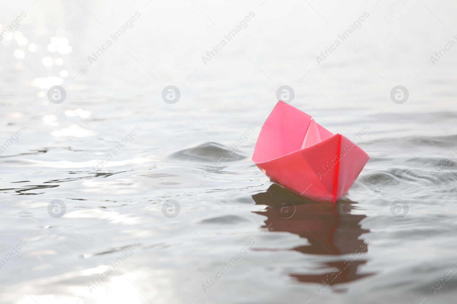 Photo of Pink paper boat on water surface, space for text