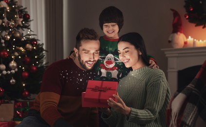 Image of Happy family opening gift box with magical light at home. Christmas celebration