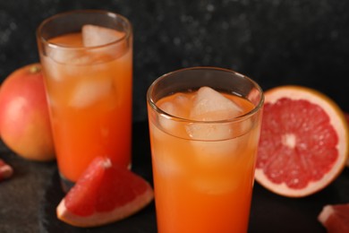 Photo of Tasty grapefruit drink with ice in glasses and fresh fruits on table, closeup
