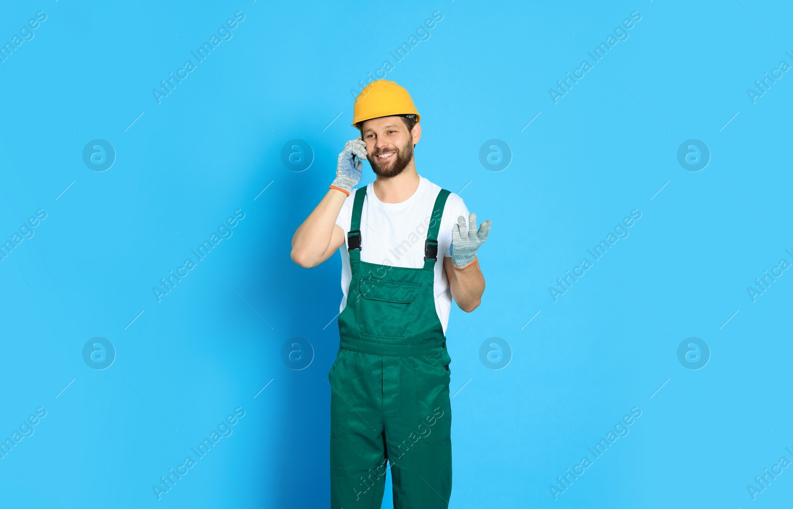 Photo of Professional repairman in uniform talking on smartphone against light blue background