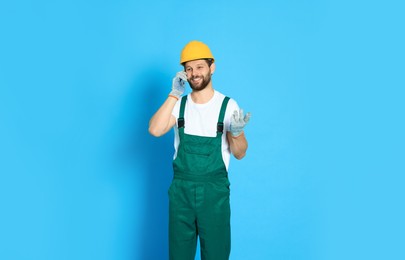 Photo of Professional repairman in uniform talking on smartphone against light blue background
