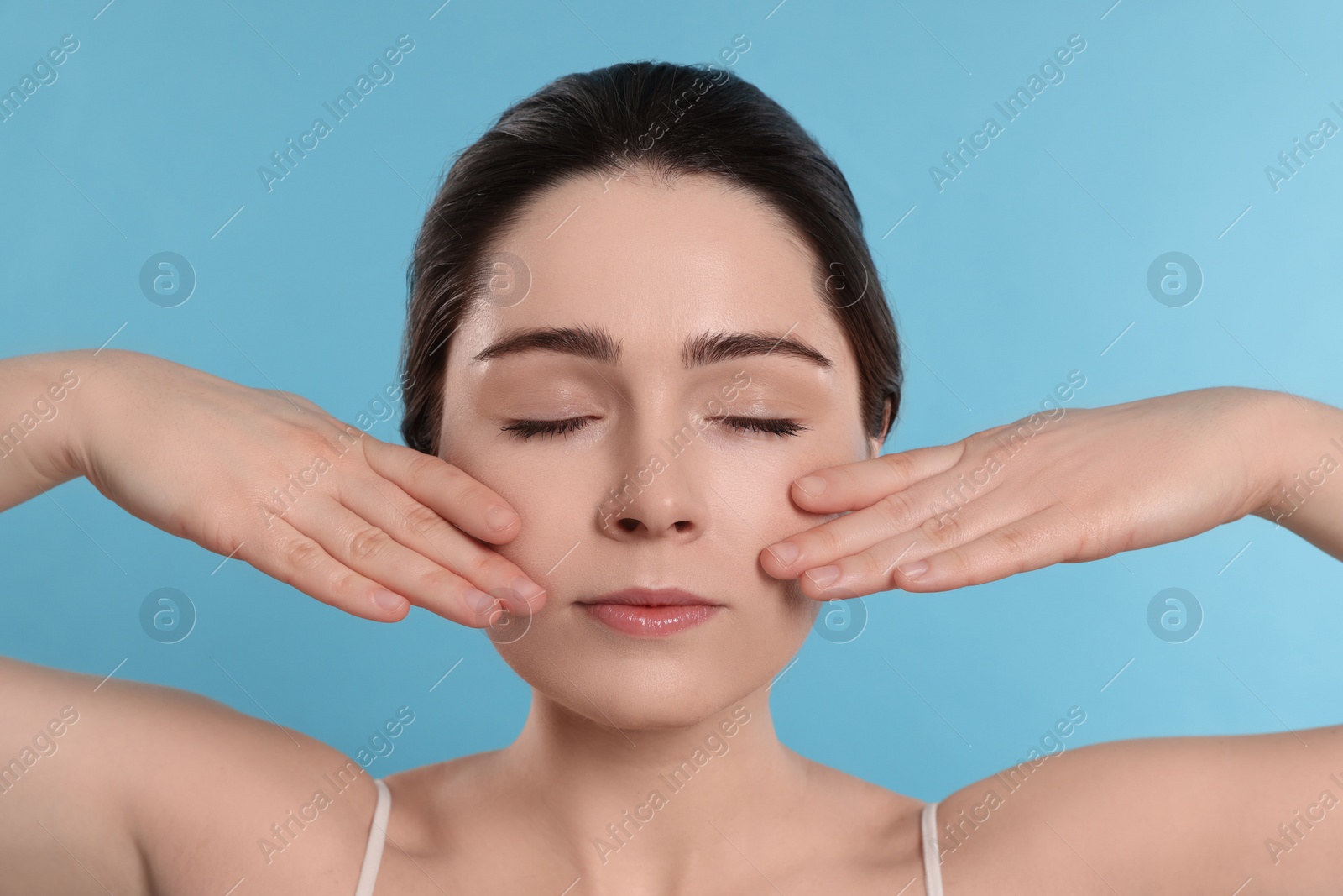 Photo of Young woman massaging her face on turquoise background