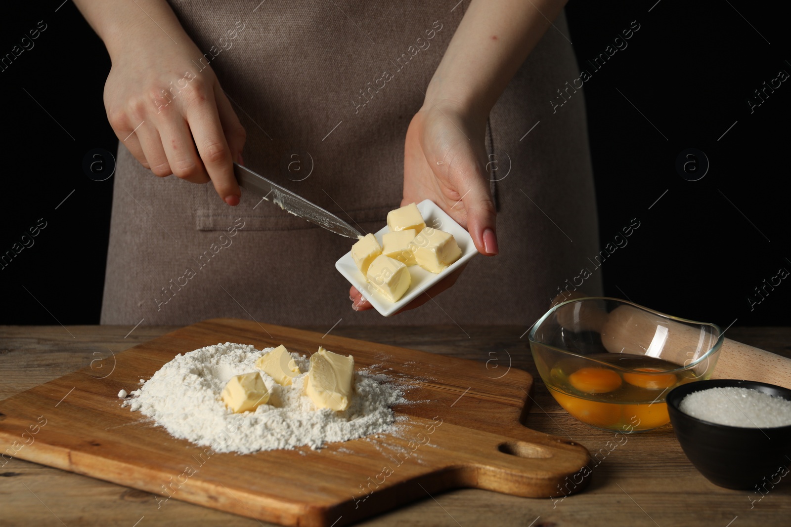 Photo of Woman adding fresh butter onto board with flour at wooden table, closeup