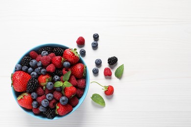 Photo of Many different fresh ripe berries in bowl on white wooden table, flat lay. Space for text