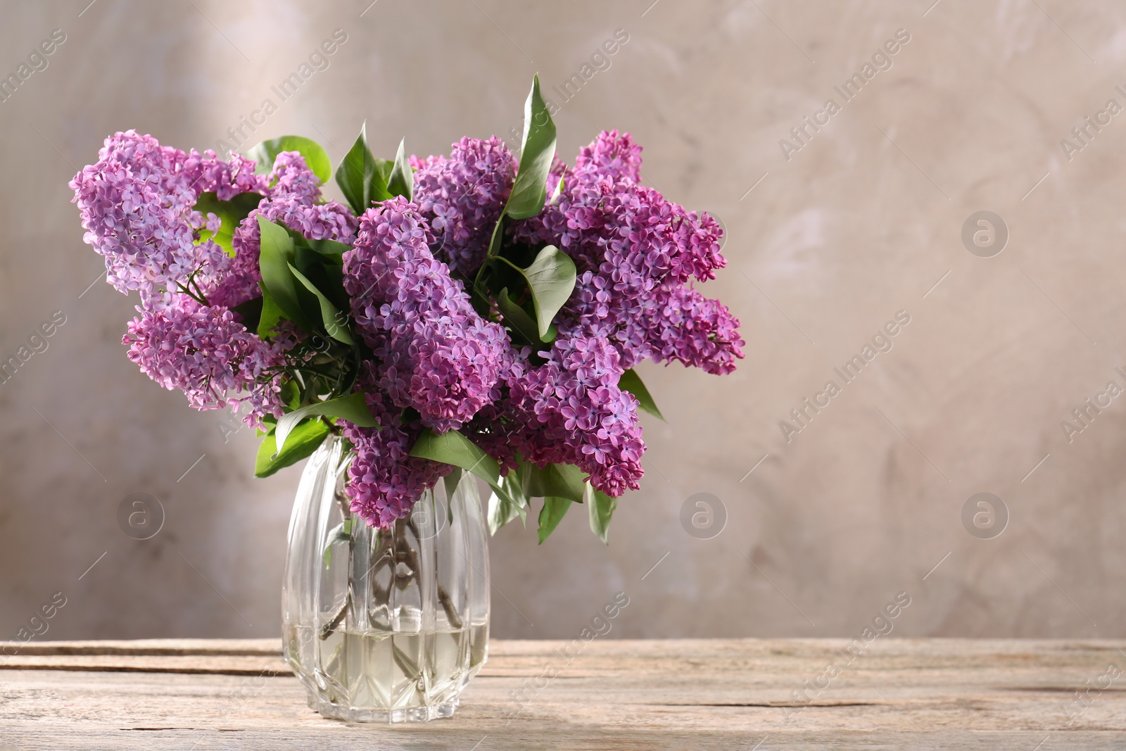 Photo of Beautiful lilac flowers in vase on wooden table, space for text