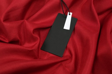 Photo of Blank black tag on red fabric. Space for text