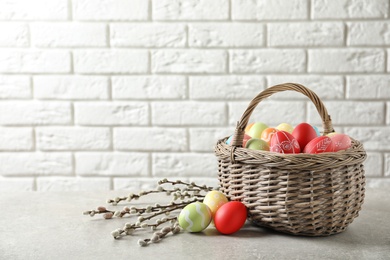 Photo of Wicker basket with colorful painted Easter eggs on table near brick wall, space for text