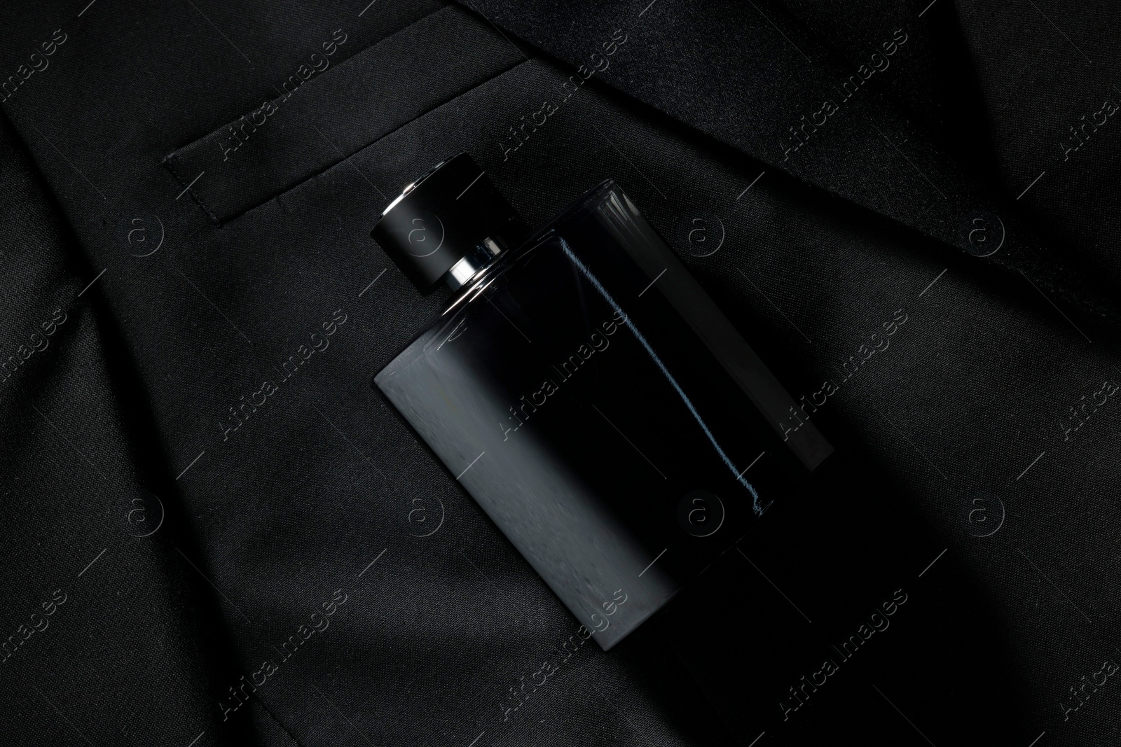 Photo of Luxury men's perfume in bottle on black jacket, top view