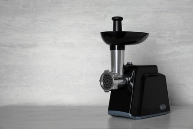 Photo of Modern electric meat grinder on light wooden table. Space for text