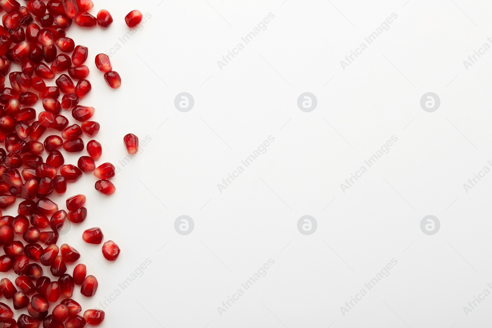 Photo of Many ripe juicy pomegranate grains on white background, flat lay. Space for text