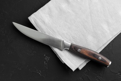 Photo of One sharp knife and napkin on dark textured table, top view