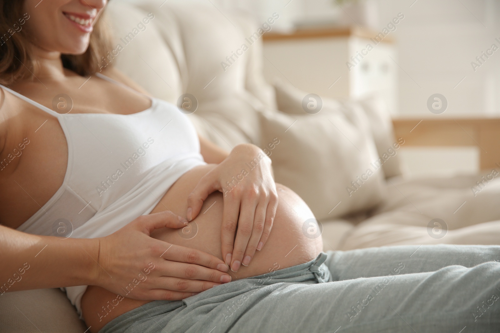 Photo of Pregnant woman making heart with her hands near belly indoors, closeup