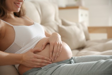 Pregnant woman making heart with her hands near belly indoors, closeup