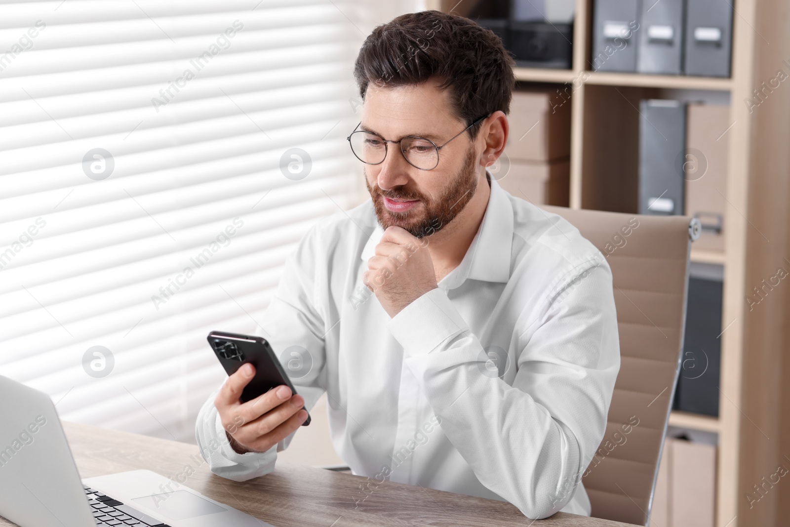 Photo of Handsome man using smartphone at table in office