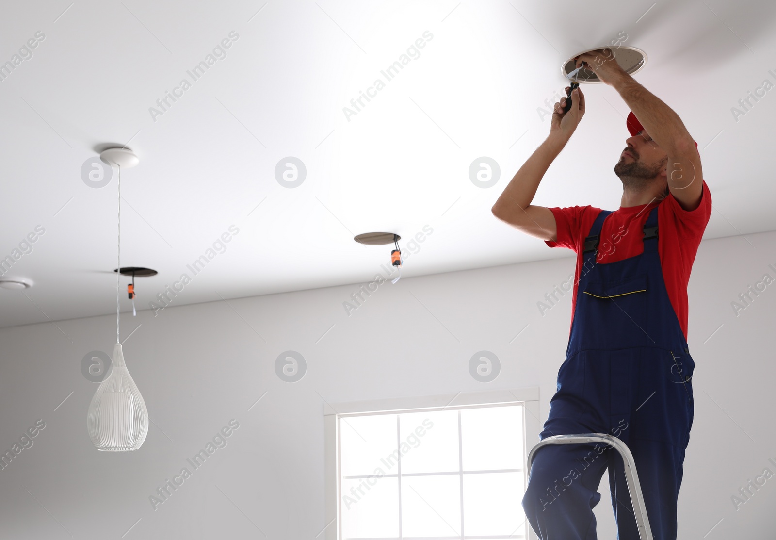 Photo of Worker installing lamp on stretch ceiling indoors. Space for text