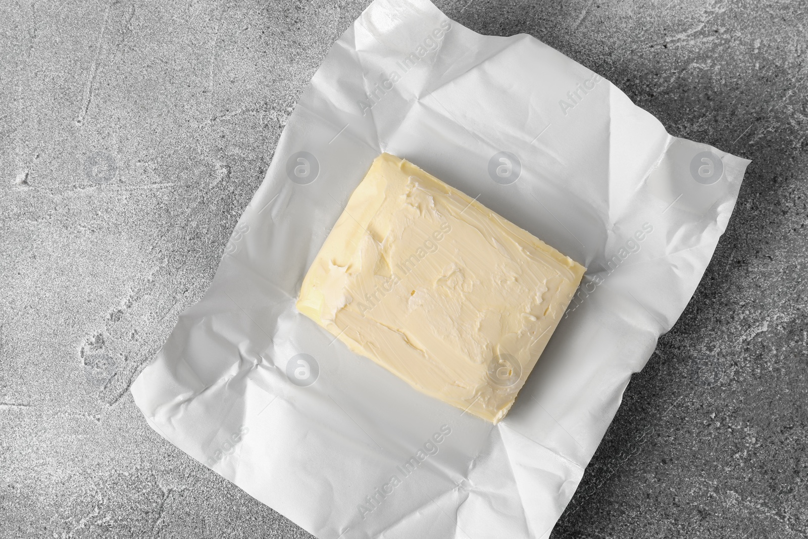 Photo of Paper wrap with piece of tasty homemade butter on grey table, top view