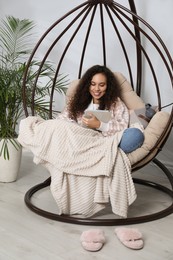 Photo of African American woman with tablet studying in egg chair at home. Distance learning