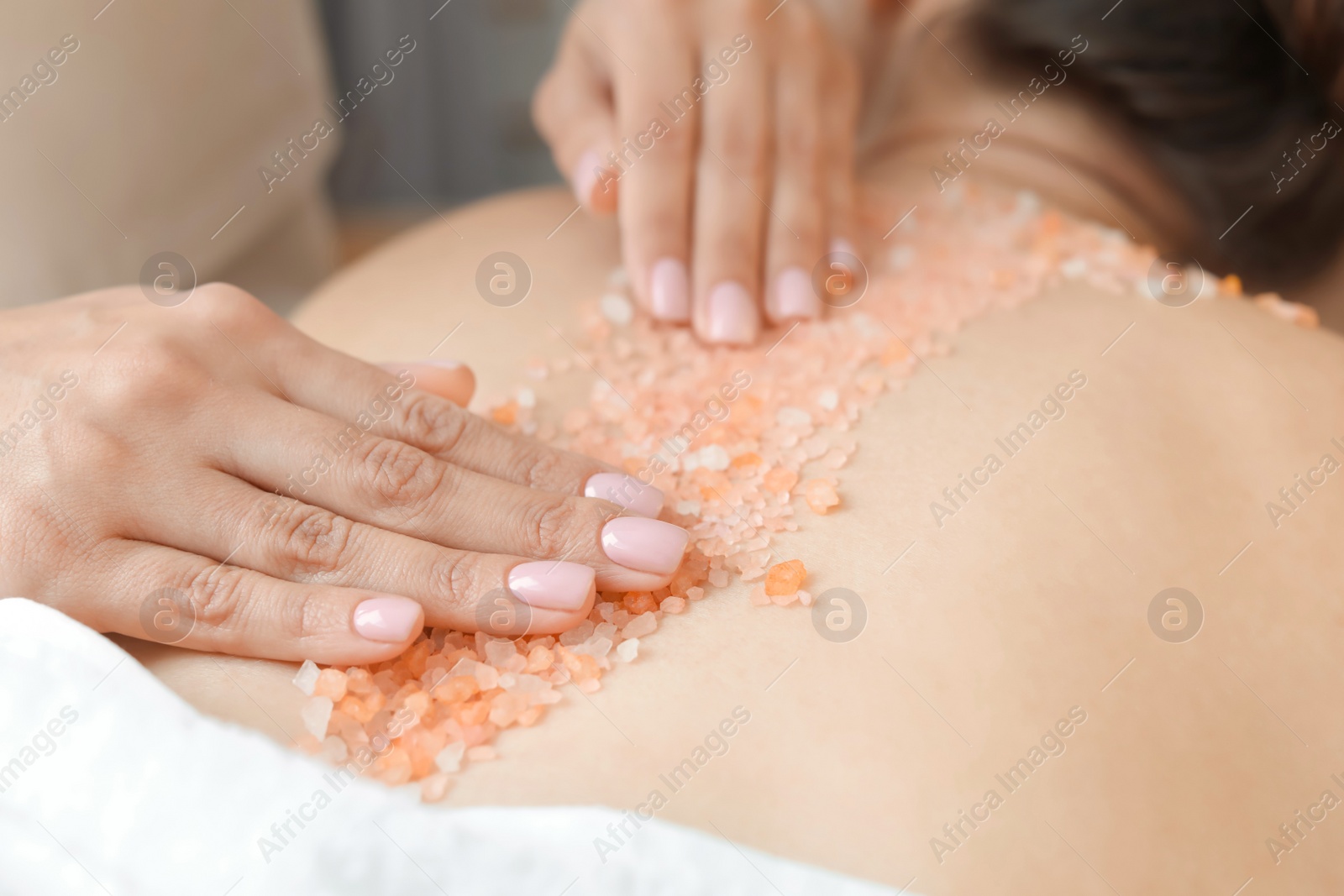 Photo of Young woman having body scrubbing procedure with sea salt in spa salon, closeup