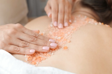 Photo of Young woman having body scrubbing procedure with sea salt in spa salon, closeup