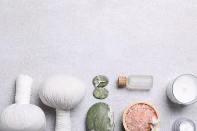 Flat lay composition with herbal massage bags and spa products on light grey table. Space for text